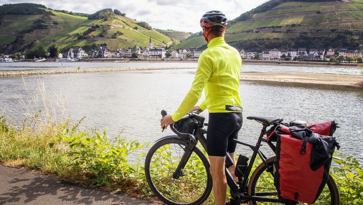 Radfahrer mit Tourenrad am Rhein vor grünen Weinbergen und malerischen Ortschaften