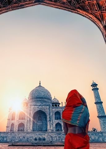 Frau im roten Sari blickt durch einen Torbogen auf das Taj Mahal in Agra, Indien