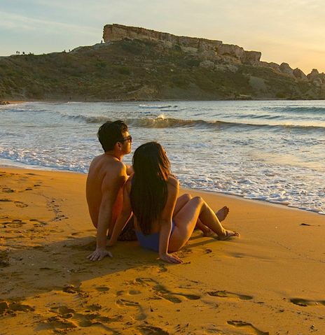 Ein Paar beobachtet den Sonnenuntergang am Strand von Ghajn Tuffieha Bay, Malta