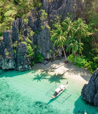 Luftaufnahme von einem kleinen Strand mit einem Boot im kristallklarem Wasser auf den Phillipinen