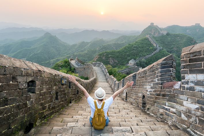 Frau sitzt mit ausgestreckten Armen auf der Großen Mauer in China und genießt den Ausblick