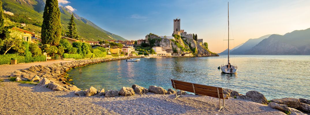 Strand in Malcesine am Gardasee mit Blick auf die Scaligerburg und Segelboot bei Sonnenuntergang