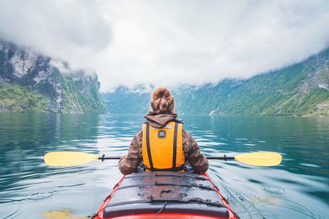 Frau paddelt im Kajak über Bergsee mit klarer Spiegelung der Gipfel