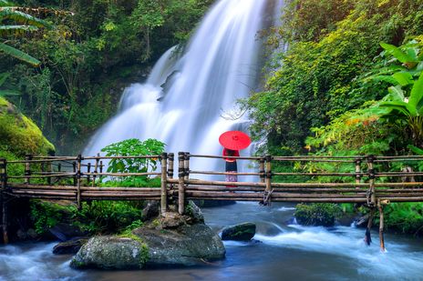 Eine Frau mit einem roten Regenschirm steht unter einem majestätischen Wasserfall in Chiang Mai, Thailand
