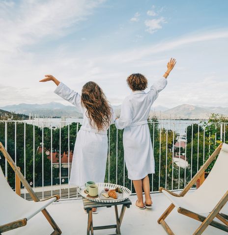 Zwei Frauen genießen den Ausblick von ihrem Hotel-Balkon auf einen Hafen