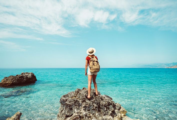 Frau steht auf einem Felsen und schaut auf das Meer