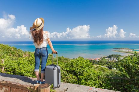 Frau mit Koffer schaut von einem Hang 