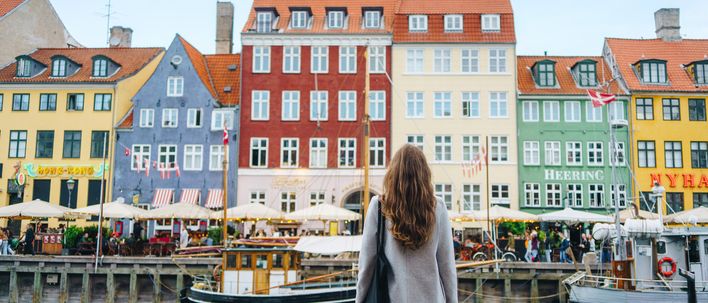 Frau steht vor einem Kanal mit Booten und bunten Häusern im Hintergrund in Kopenhagen