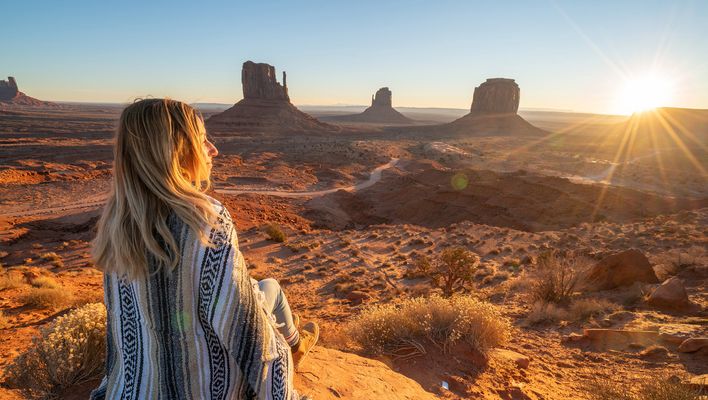 Frau in Rückansicht blickt über das Monument Valley in Arizona in den USA in den Sonnenuntergang
