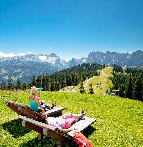 Frau sitzt auf Bank und guckt in die Berge