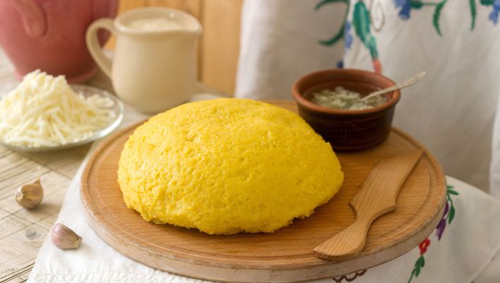 Rumänische Mămăligă aus Maisgrieß wird mit geriebenem Käse und cremiger Beilage auf einem Holzbrett serviert