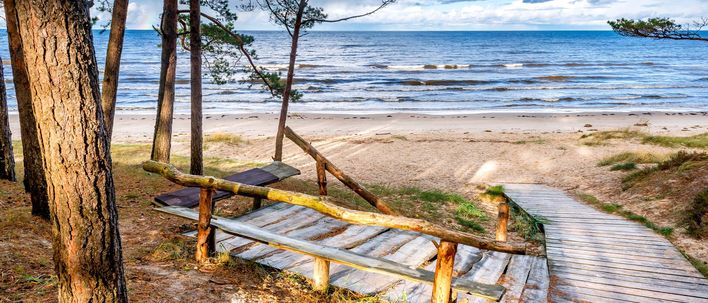Blick über einen Holzsteg durch Bäume auf Strand und Meer von Jurmala in Lettland