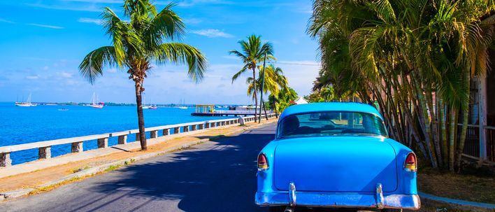 Blauer Oldtimer auf einer Küstenstraße mit Palmen umsäumt in Varadero auf Kuba