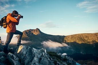 Mann steht auf einem Berg und fotografiert die Landschaft