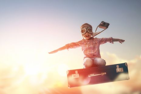 Kind mit Fliegerbrille auf fliegendem Koffer