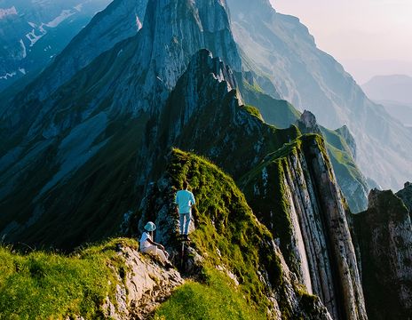 Ein Wanderer steigt über einen schmalen Berggrat im Appenzellerland mit steilen Felswänden und weitem Ausblick.