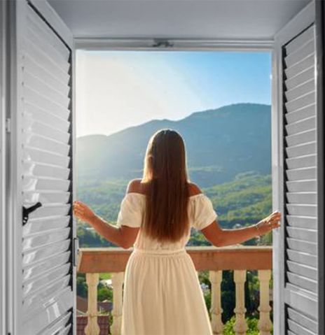 Eine Frau in Farbe schaut aus einem Fenster in schwarz-weiß in eine bergige farbige Landschaft