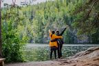 Zwei Reisende stehen am Seeufer in Jyväskylä, Finnland, und blicken auf die bewaldete Landschaft