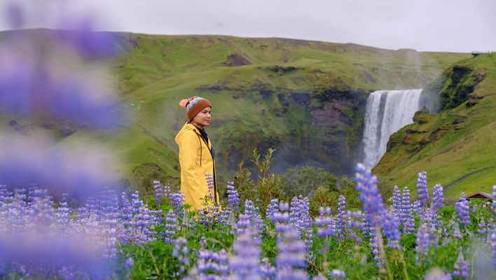 Frau mit einem gelben Regenmantel steht vor dem Wasserfall Skogafoss in Island