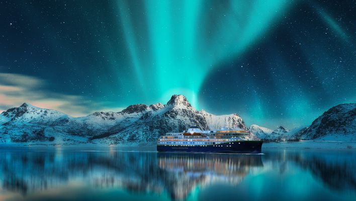Kreuzfahrtschiff vor verschneiten Bergen unter dem Nordlicht
