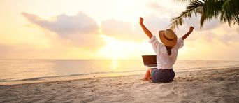 Frau sitzt am Strand mit einem Laptop und freut sich