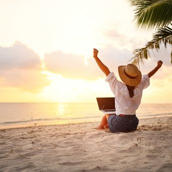 Frau sitzt im Sand und hat einen Laptop auf dem Schoß