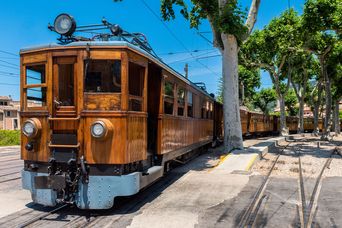 Historische Straßenbahn fährt durch eine sonnige Straße in Sóller auf Mallorca