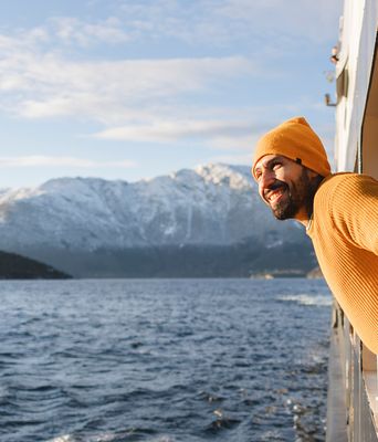 Ein lächelnder Mann lehnt sich aus einem Schiff und bewundert die wunderschöne verschneite Berglandschaft