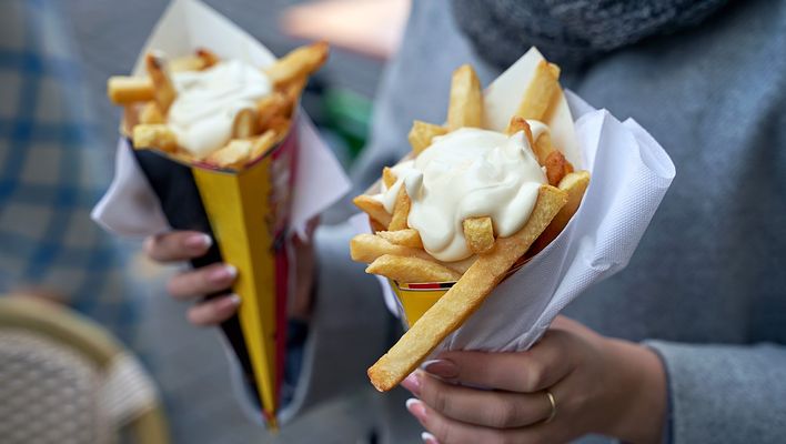 Zwei Portionen Belgische Pommes frites mit Mayonnaise werden in Papiertüten auf einem Markt serviert