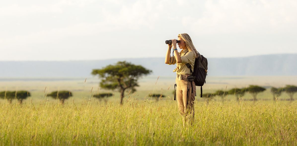 Frau mit Fernglas auf Safari in Steppe