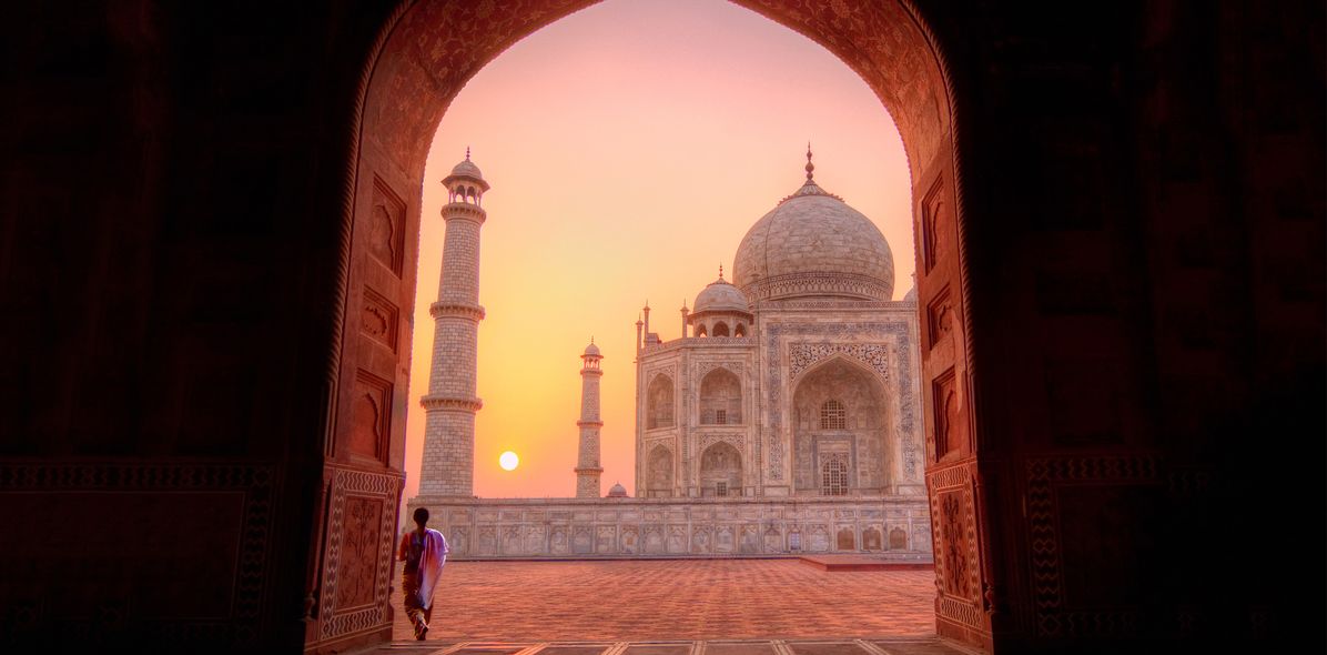 Frau steht beim Sonnenuntergang in einem Torbogen mit Blick auf den Taj Mahal, Indien