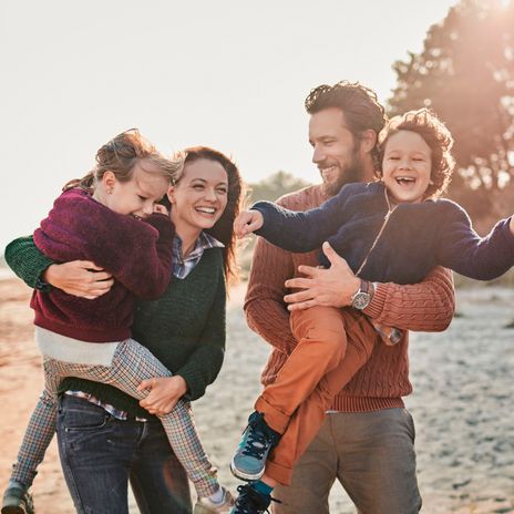 Eltern mit Kindern im Arm laufen fröhlich im Herbst am Strand entlang