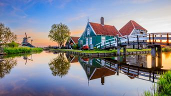 Idyllische Dorfkulisse mit Windmühle, Holzhäusern und spiegelndem Kanal in Zaanse Schans, Niederlande