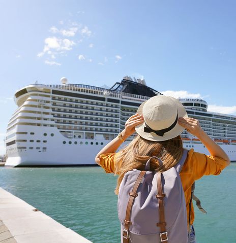 Frau steht vor einem Kreuzfahrtschiff an der Anlegestelle