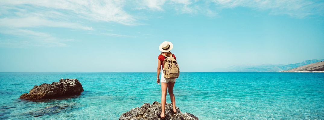 Frau steht auf Felsen am Meer und blickt in die Ferne bei klarem Himmel
