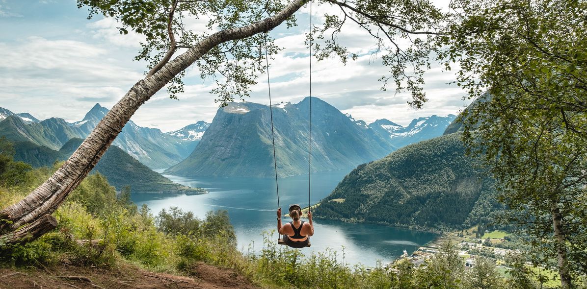 Frau in Hjørundfjord schaukelt an einem Baum und blickt auf den Fjord