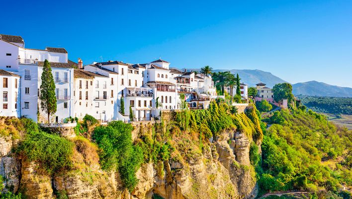 Weiß getünchte Häuser von Ronda auf einem Felsen mit grüner Landschaft im Hintergrund