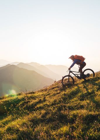 Mountainbiker fährt bergauf auf einem schmalen Trail bei Sonnenuntergang