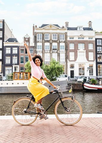 Frau fährt mit dem Fahrrad entlang einer Gracht in Amsterdam