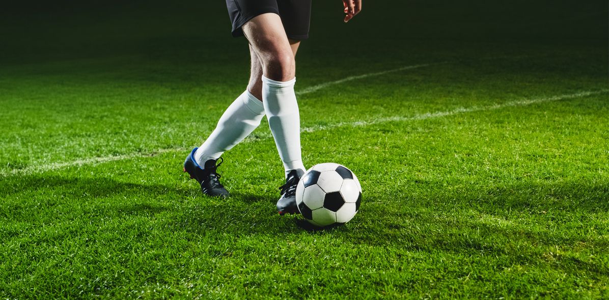 Ein Fußballspieler schießt den Ball über die grüne Wiese