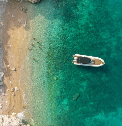 Luftaufnahme von einem Boot am Strand von Kroatien mit Menschen im Wasser