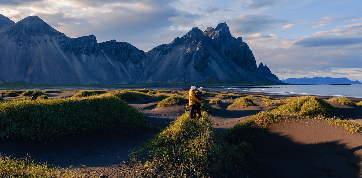 Paar in der Landschaft von Stokksnes auf Island bei Sonnenschein mit Dünen, Strand und Bergkulisse