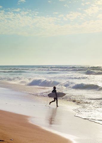 Person mit einem Surfbrett an einem Strand an der Algarve