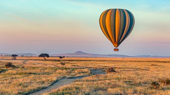 Heißluftballon fliegt bei Sonnenaufgang über den Serengeti Nationalpark in Tansania
