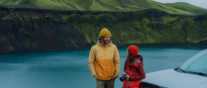 Paar neben einem Mietwagen an einem türkisblauen See auf Island