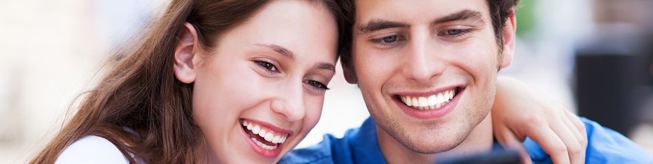 Frau und Mann gucken Arm in Arm interessiert in ein Handy und lachen