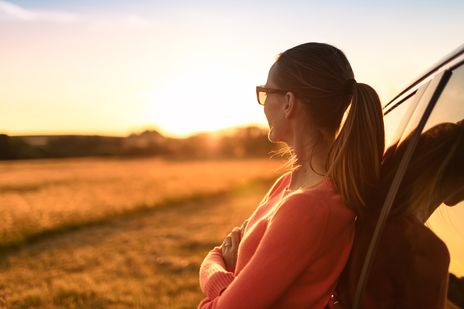 Frau vor Auto beim Sonnenuntergang