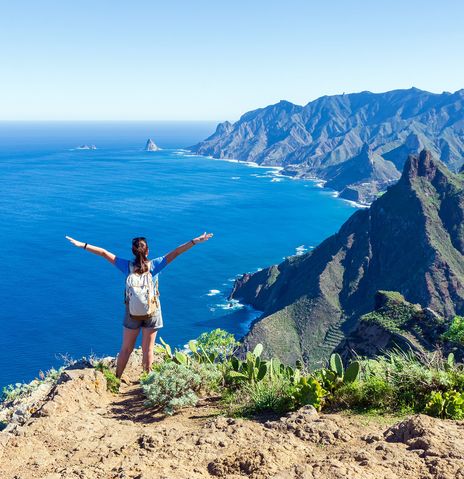 Frau an Klippe mit Blick auf Meer und Berge