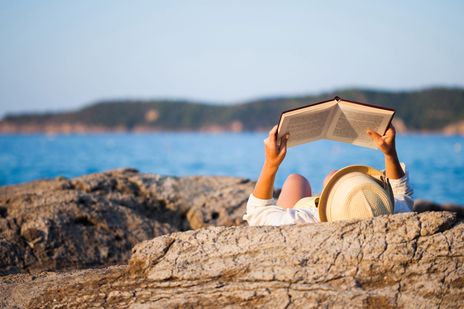 Frau auf Felsen am Meer mit Buch