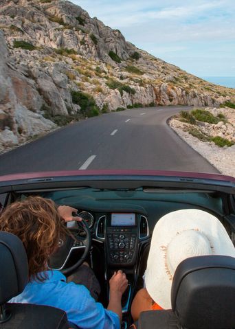 Personen fahren im Cabrio am Cap de Formentor eine Küstenstraße entlang, Blick aufs Meer